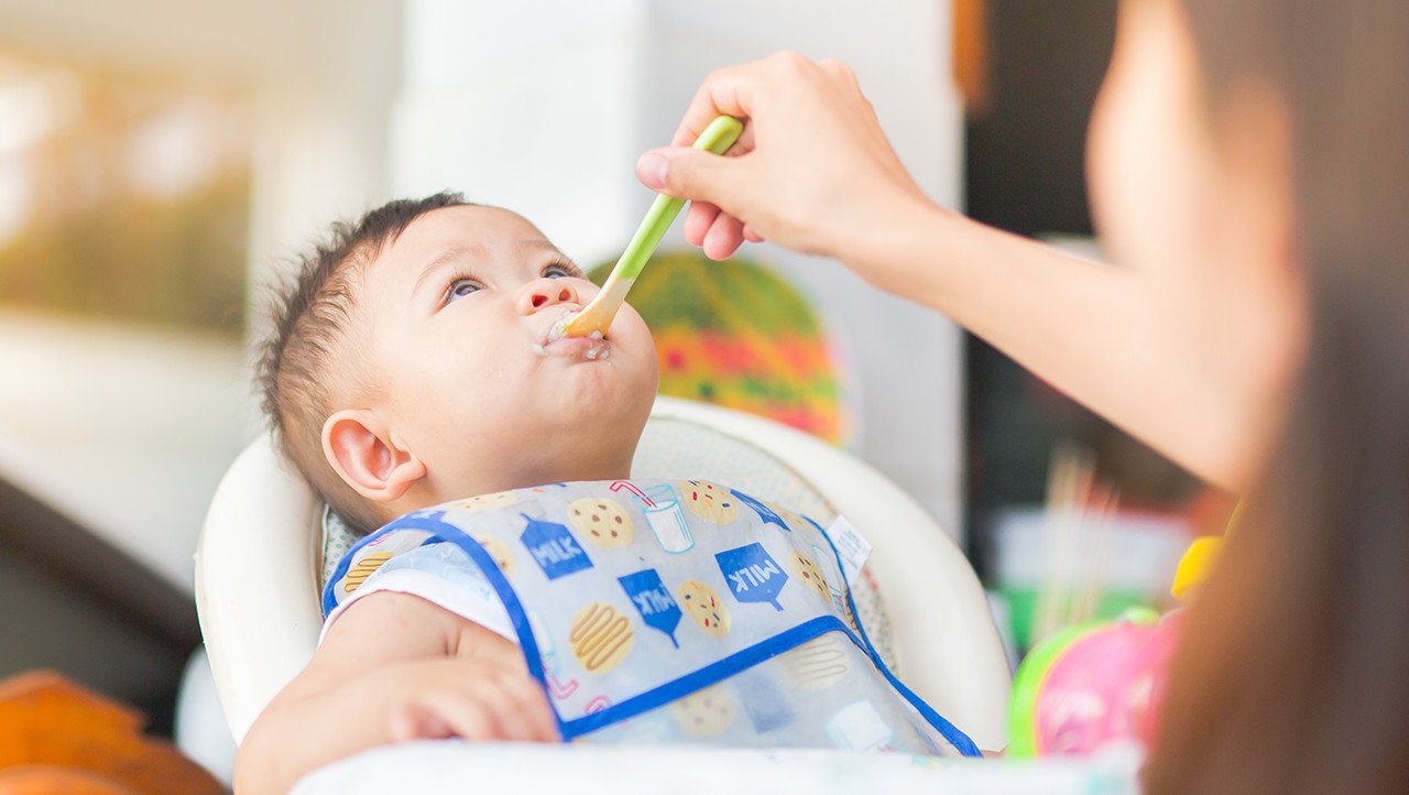 Bebé en una silla alta siendo alimentado con cuchara